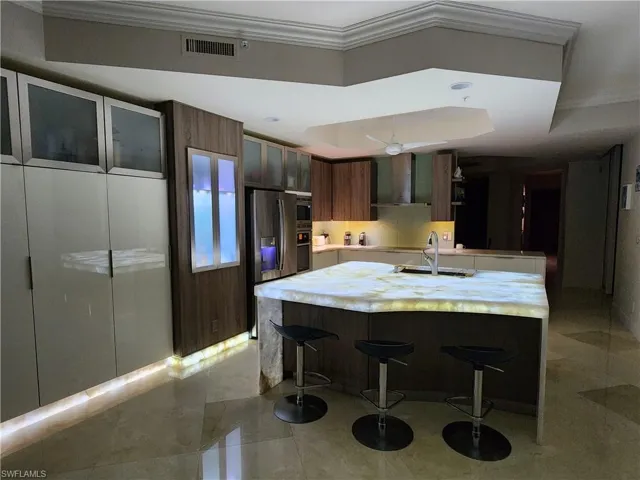 Kitchen with a breakfast bar area, sink, crown molding, wall chimney range hood, and a tray ceiling