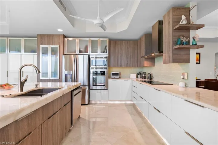Kitchen featuring sink, a raised ceiling, wall chimney range hood, white cabinetry, and appliances with stainless steel finishes