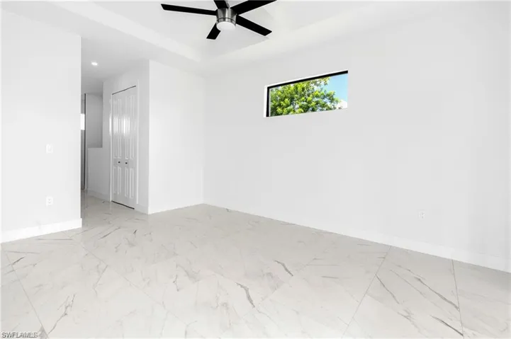 Unfurnished room featuring a ceiling fan, a raised ceiling, marble finish floors, and recessed lighting