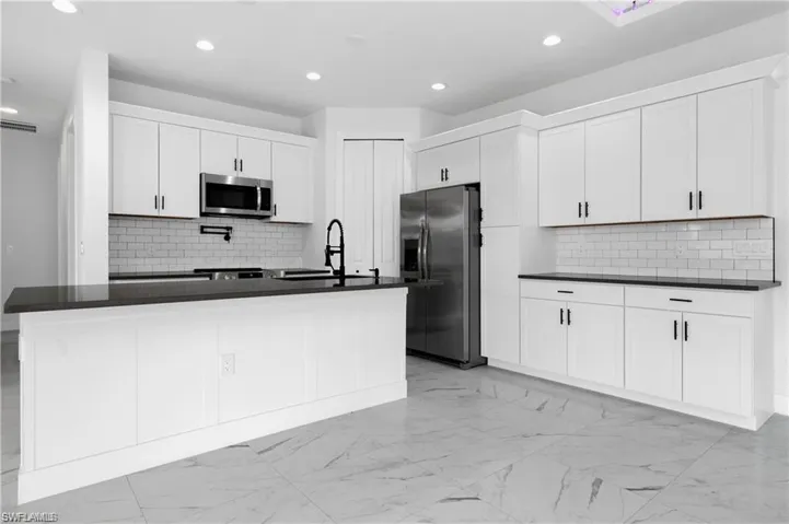 Kitchen with appliances with stainless steel finishes, dark countertops, tasteful backsplash, and recessed lighting