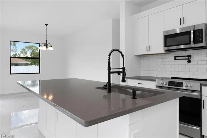 Kitchen featuring stainless steel appliances, backsplash, white cabinetry, light marble finish floors, and an island with sink