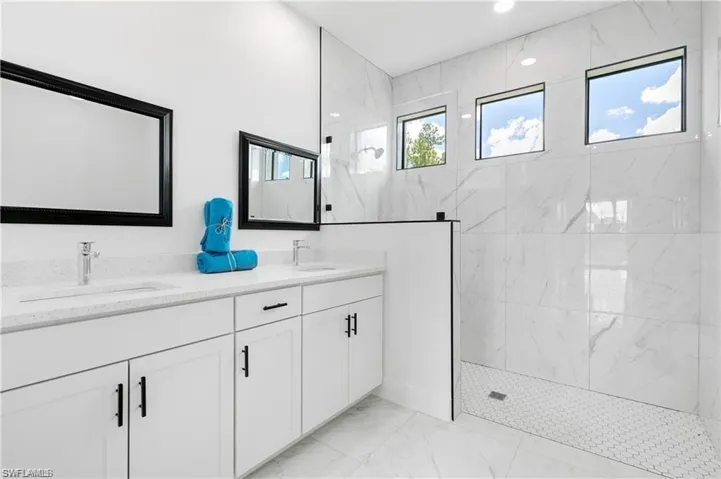 Bathroom featuring marble look tile flooring, a marble finish shower, and double vanity