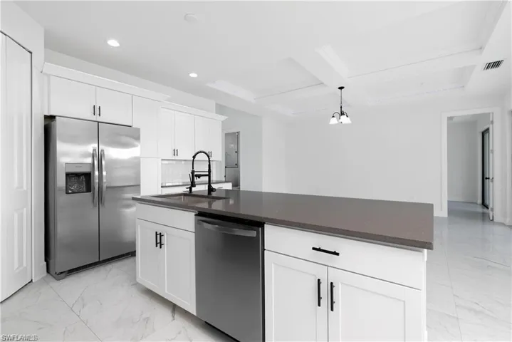Kitchen with appliances with stainless steel finishes, light marble finish flooring, coffered ceiling, recessed lighting, and dark countertops