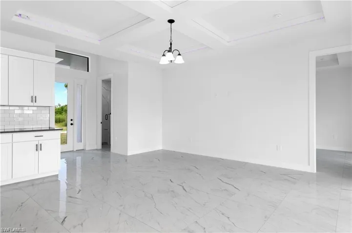 Unfurnished dining area featuring a chandelier, coffered ceiling, light marble finish floors, and beamed ceiling