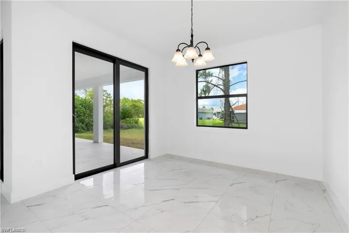 Unfurnished room featuring marble look tiles, plenty of natural light, and a chandelier