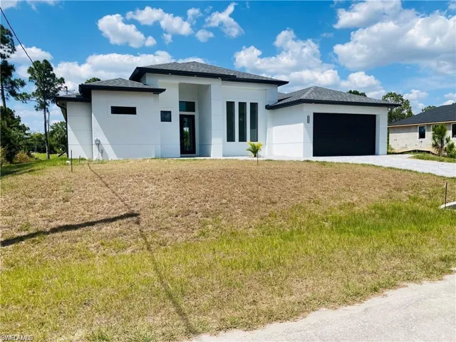 Prairie-style home featuring a garage, driveway, stucco siding, and a front yard