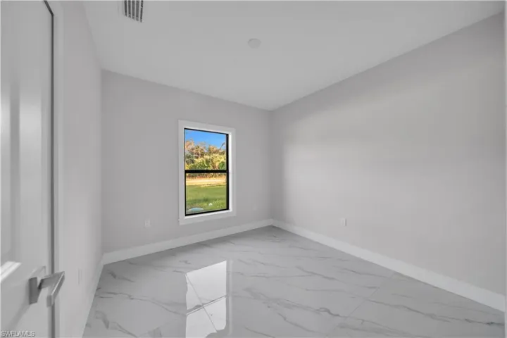 Light-filled room featuring large format marble-look tile flooring, crisp white baseboards, and a single window with a white frame