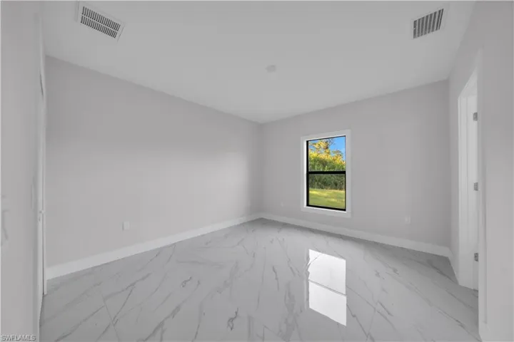 Spacious room featuring large format tile flooring, a window with exterior landscaping, white baseboards, and light gray walls