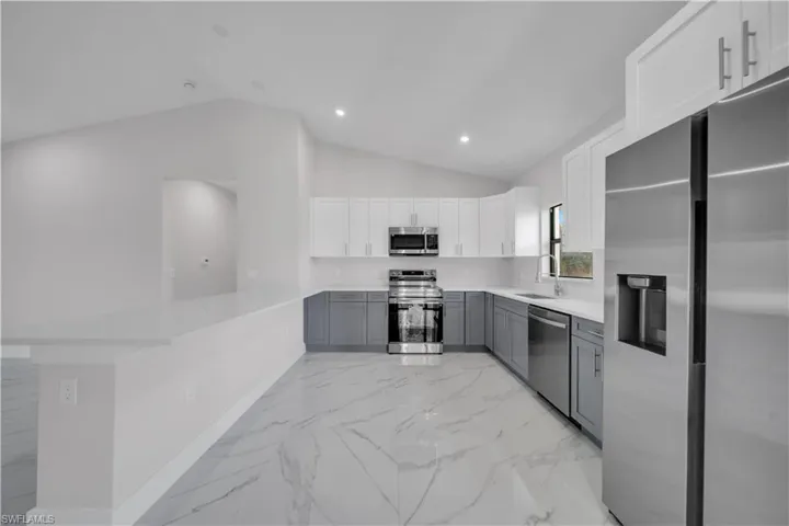 Contemporary kitchen featuring two-tone cabinetry, stainless steel appliances, a breakfast bar, recessed lighting, and large format tile flooring