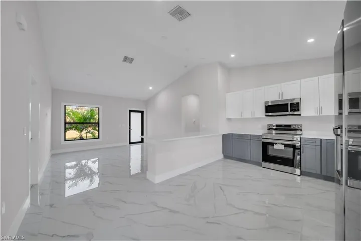 Spacious kitchen and living area featuring a vaulted ceiling, glossy tile flooring, two-tone cabinetry, stainless steel appliances, and recessed lighting