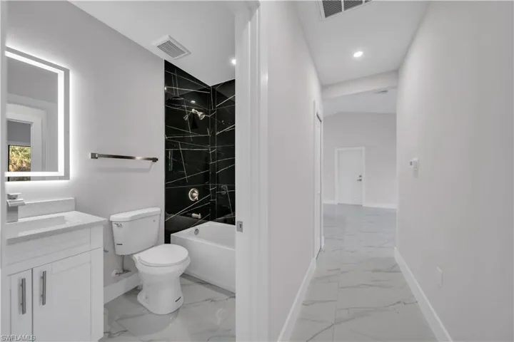 Bathroom featuring a white vanity with integrated sink, illuminated mirror, and a black patterned shower surround with a white bathtub