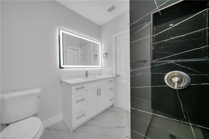 Modern bathroom featuring a black tiled shower with an integrated niche, a white vanity with brushed nickel hardware, and an illuminated mirror