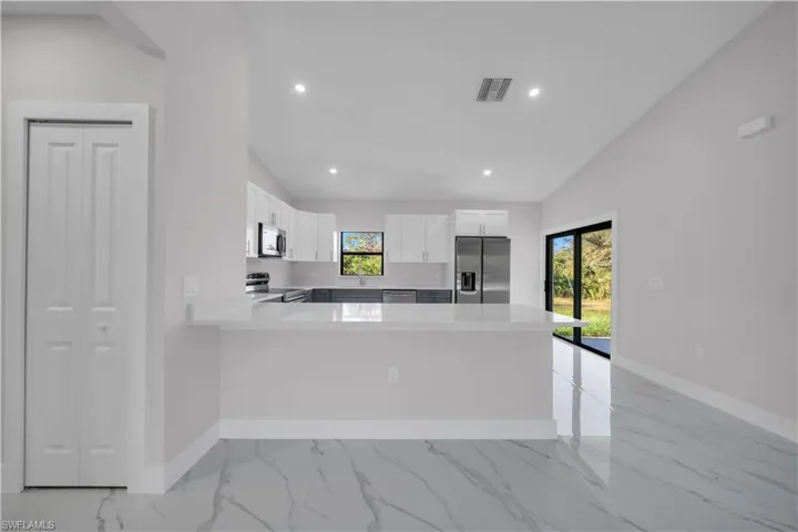 Kitchen featuring white shaker cabinetry, stainless steel appliances, a white stone countertop breakfast bar, and recessed lighting