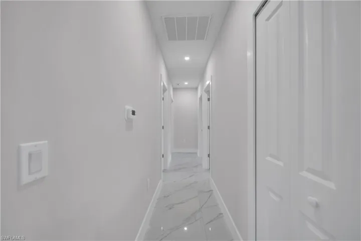 Hallway featuring polished tile flooring, recessed lighting, white paneled doors, and a neutral wall palette