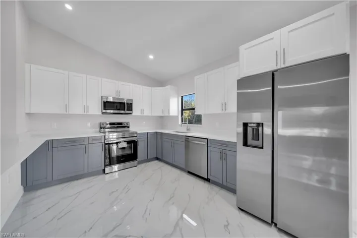 Kitchen featuring two-tone cabinetry, stainless steel appliances, a vaulted ceiling, recessed lighting, and white marble-look flooring