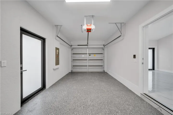 Spacious garage featuring a durable speckled epoxy floor, white painted walls, and a roll-up garage door with an automatic opener