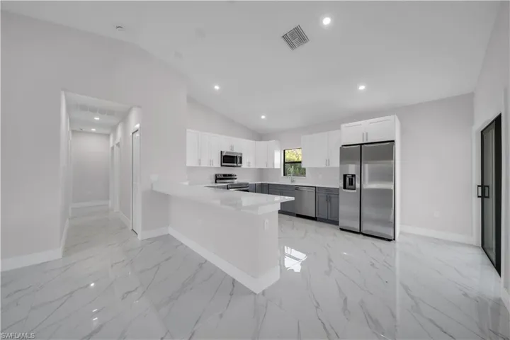Modern kitchen featuring a breakfast bar, stainless steel appliances, two-tone cabinetry, and a window for natural light