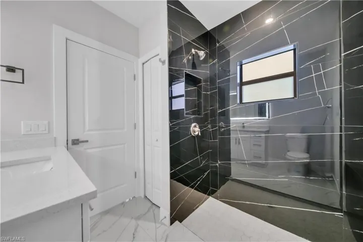 Walk-in shower featuring black tile with white veining, a built-in niche, and a window