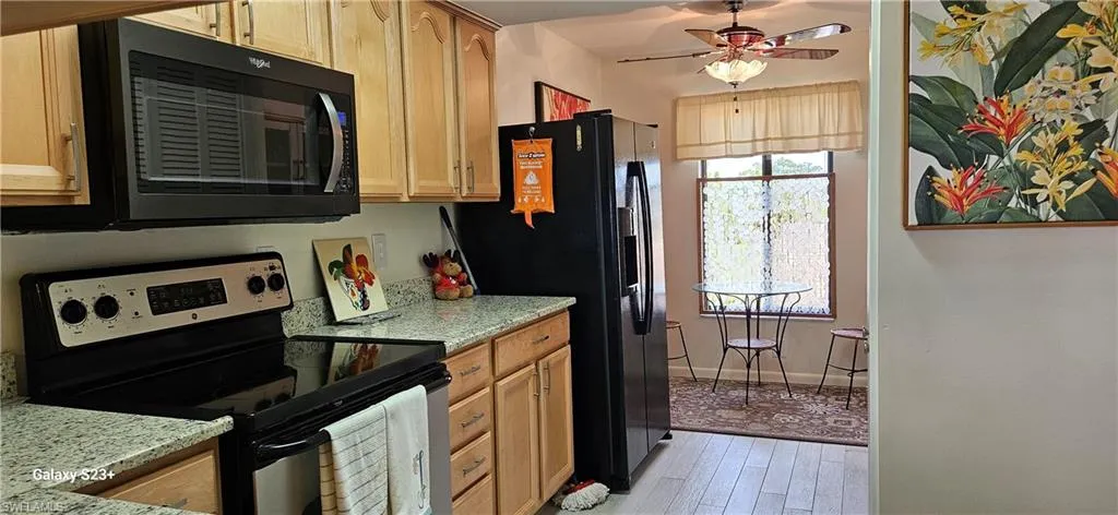 Kitchen featuring black appliances, ceiling fan, light wood finished floors, light stone counters, and light brown cabinets