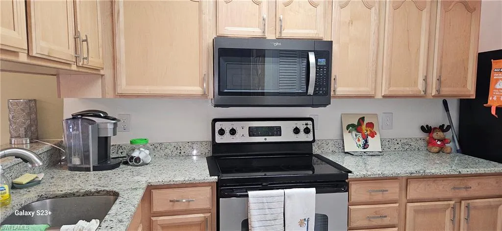 Kitchen with stainless steel electric range oven, light brown cabinetry, light stone counters, and refrigerator