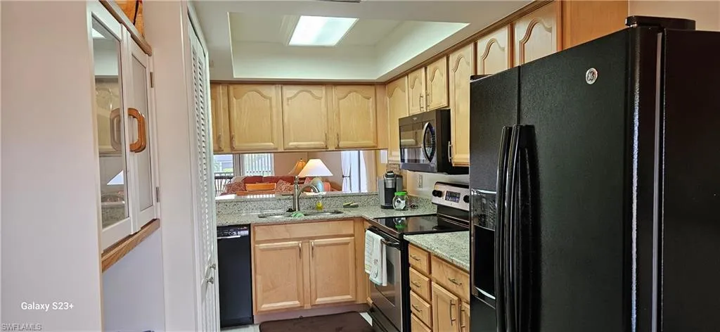 Kitchen with black appliances, light brown cabinetry, and light stone countertops