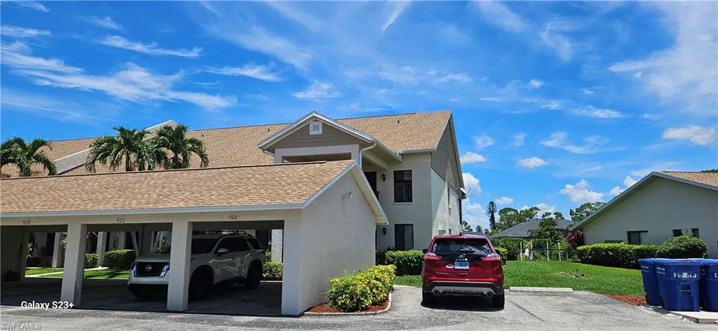 View of front of property featuring covered and uncovered parking, a shingled roof, stucco siding, and a front yard