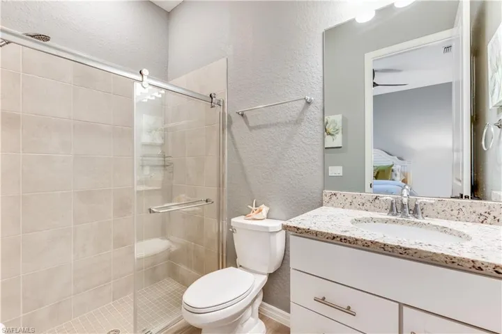 Bathroom with ceiling fan, a shower with shower door, toilet, and large vanity