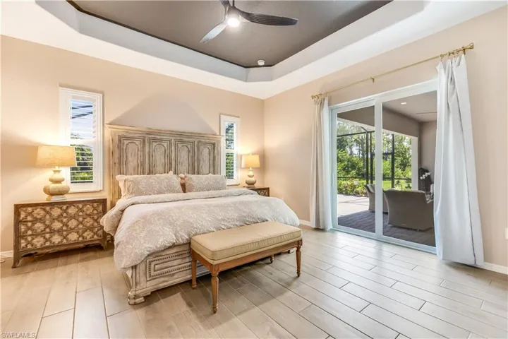 Bedroom featuring multiple windows, ceiling fan, a tray ceiling, and access to outside