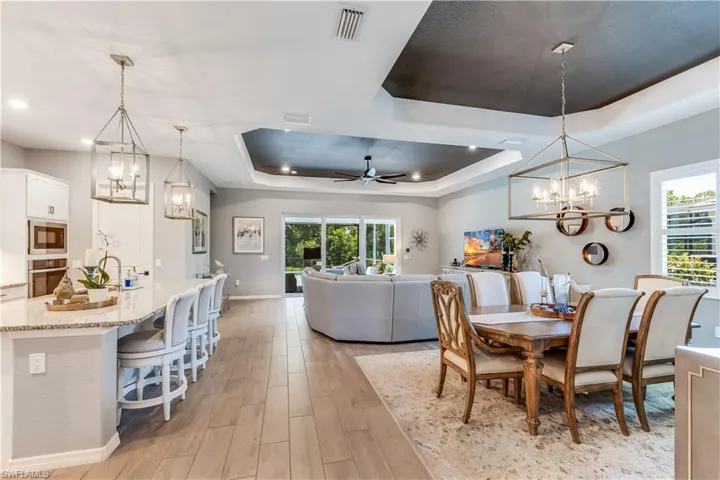 Dining space with light hardwood / wood-style floors, sink, a tray ceiling, and ceiling fan with notable chandelier