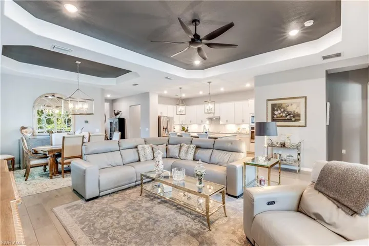 Living room featuring a tray ceiling, light wood-type flooring, and ceiling fan with notable chandelier