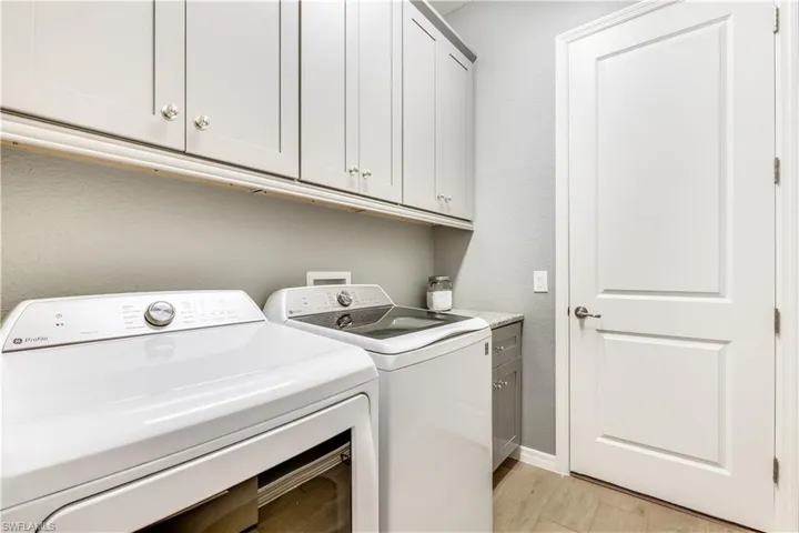 Laundry area with light hardwood / wood-style flooring, washing machine and clothes dryer, and cabinets