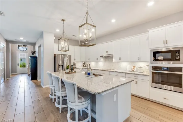 Kitchen featuring appliances with stainless steel finishes, white cabinets, a kitchen island with sink, and backsplash