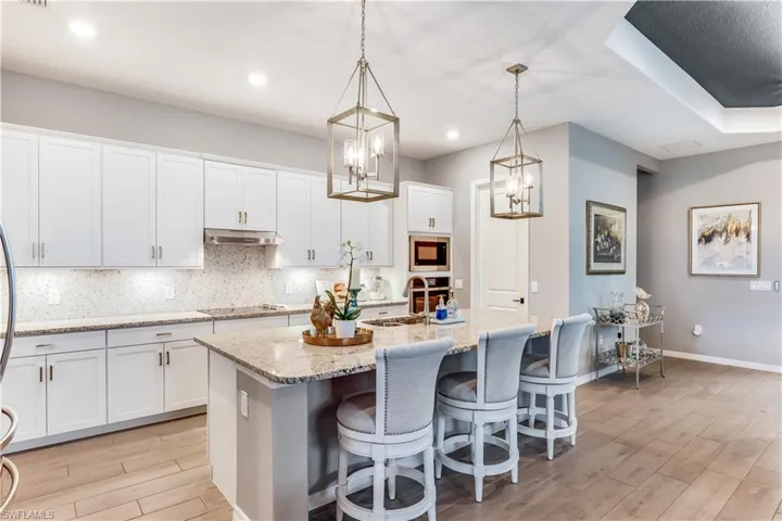 Kitchen with decorative light fixtures, white cabinetry, tasteful backsplash, and stainless steel microwave