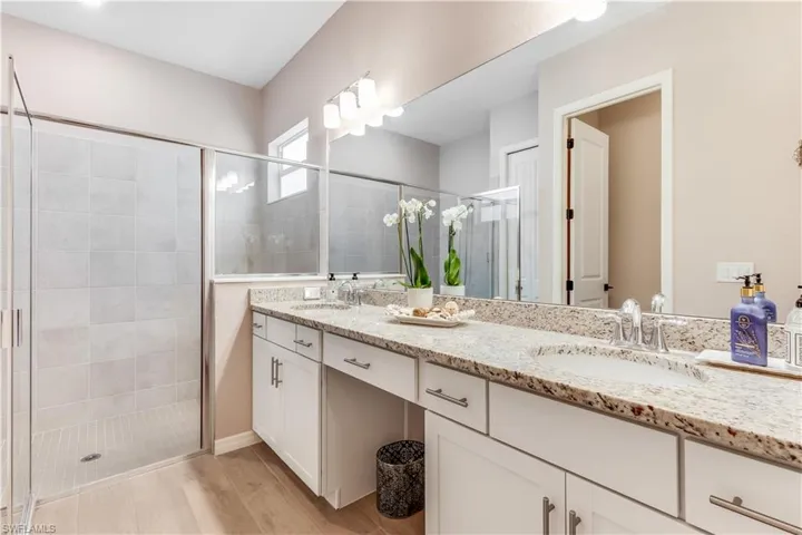 Bathroom with wood-type flooring, a shower with shower door, large vanity, and dual sinks