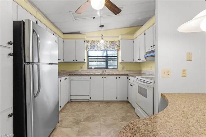 Kitchen with under cabinet range hood, hanging light fixtures, white appliances, a ceiling fan, and a sink
