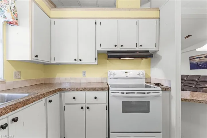 Kitchen with white cabinetry, a sink, under cabinet range hood, and white range with electric cooktop
