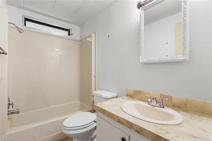 Bathroom with toilet, a textured ceiling,  shower combination, vanity, and a textured wall