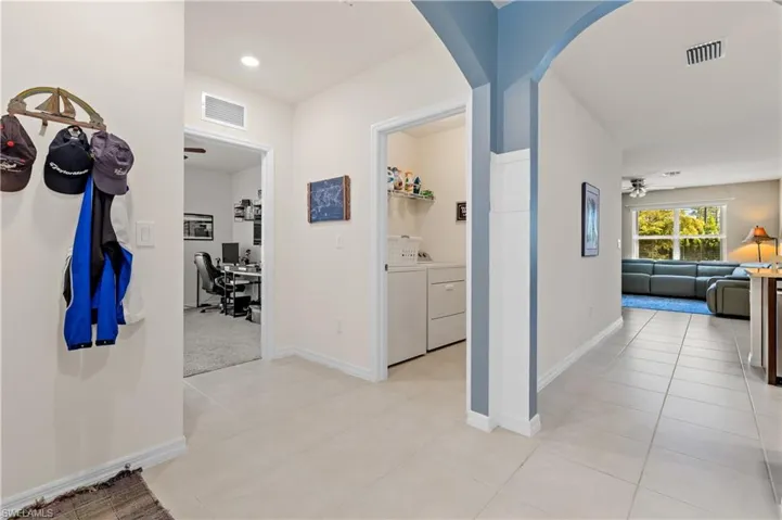 Hall featuring a desk, washing machine and dryer, light tile patterned floors, and arched walkways