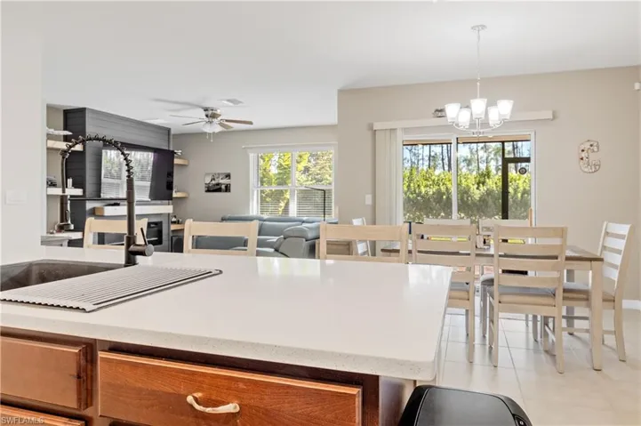 Kitchen with light stone countertops, a chandelier, ceiling fan, light tile patterned flooring, and open floor plan