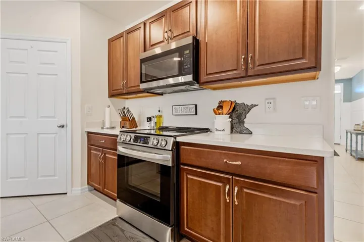Kitchen with stainless steel appliances, light tile patterned floors, wood finish cabinets, and light stone counters