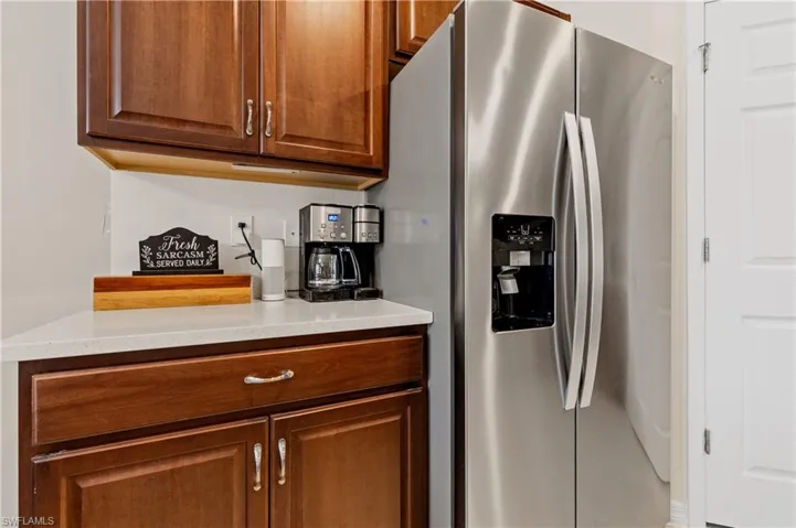 Kitchen with stainless steel fridge with ice dispenser, wood finish cabinets, and light stone counters