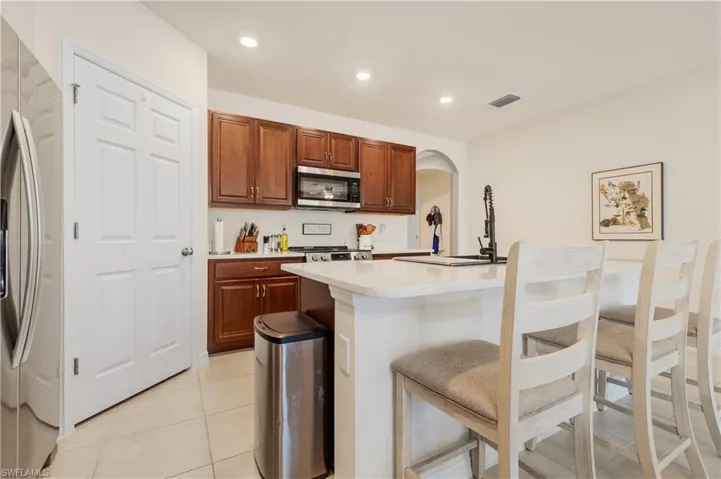 Kitchen with arched walkways, stainless steel appliances, a kitchen bar, an island with sink, and light tile patterned floors