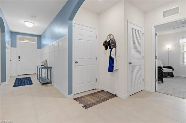 Foyer entrance featuring arched walkways, light tile patterned flooring, and wainscoting
