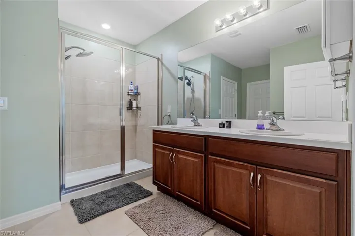 Bathroom with double vanity, a stall shower, and light tile patterned floors