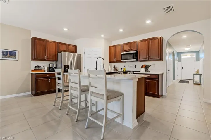 Kitchen with arched walkways, a breakfast bar area, a kitchen island with sink, stainless steel microwave, and light tile patterned flooring