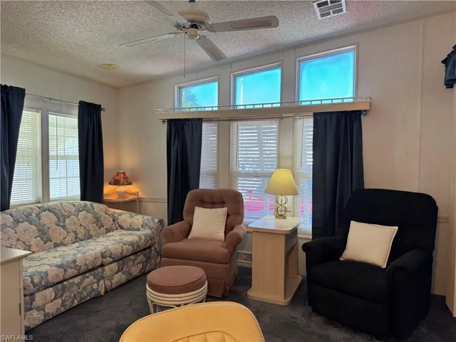 Carpeted living area featuring visible vents, a textured ceiling, and a ceiling fan