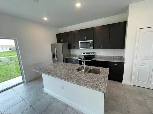 Kitchen featuring a center island with sink, light tile patterned floors, light stone countertops, and appliances with stainless steel finishes