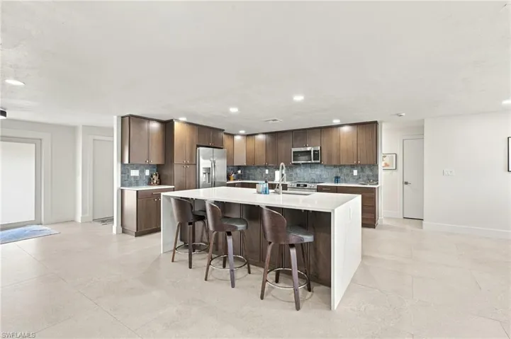 Gourmet kitchen featuring a large central island with seating, stainless steel appliances, dark wood cabinetry, a tile backsplash, and light-toned tile flooring