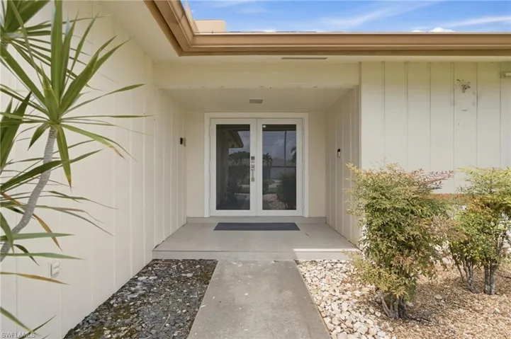 Entryway with concrete path, dual glass-paneled doors, and exterior lighting