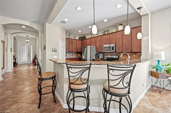 Kitchen with appliances with stainless steel finishes, pendant lighting, kitchen peninsula, light tile patterned floors, and decorative backsplash